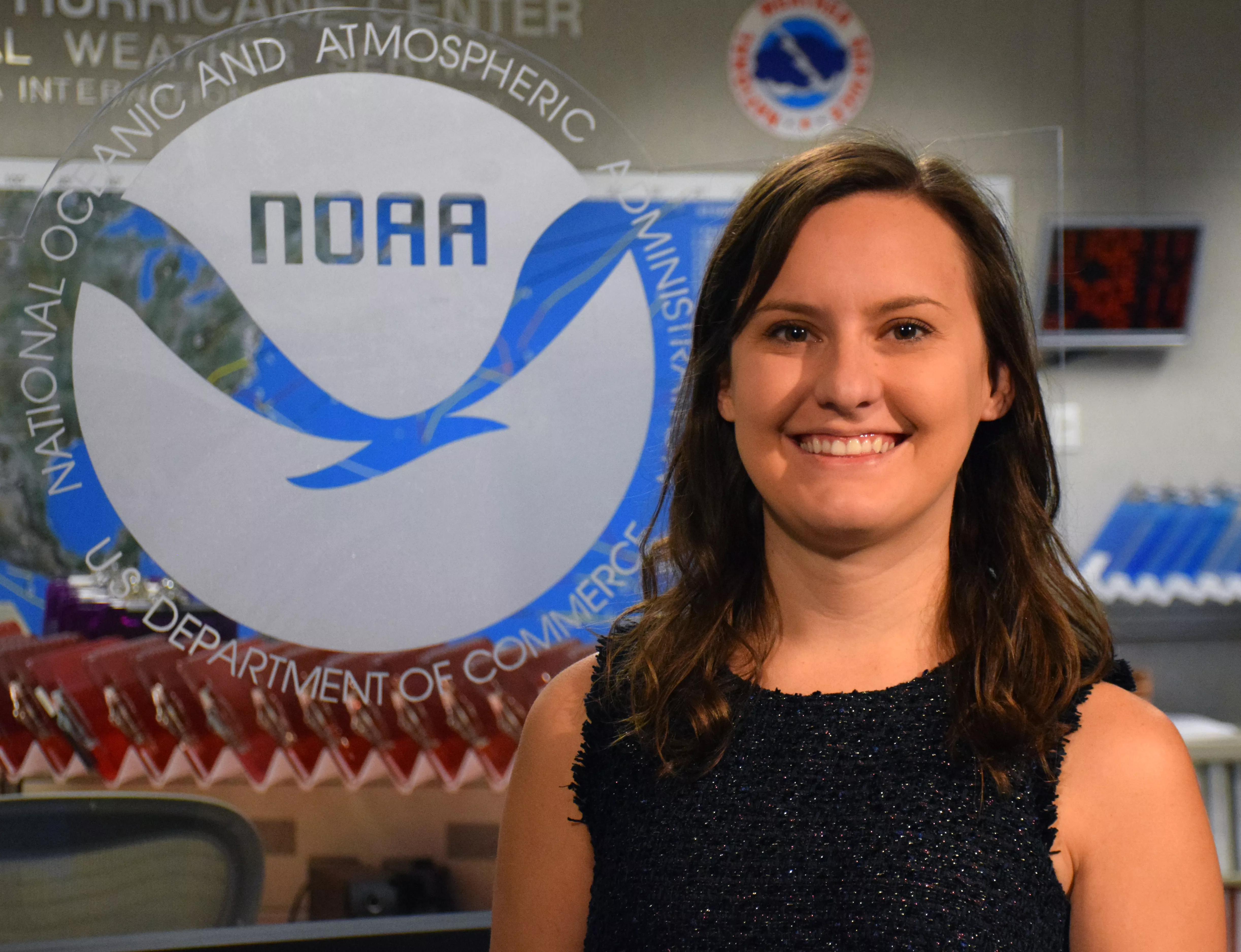 Headshot of Dr. Stephanie Stevenson in front of a glass window with the NOAA logo to her left