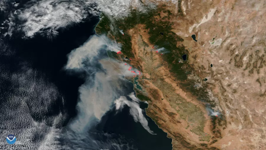 A satellite image of California showing fires in the northern part of the state as red hotspots and thick smoke billowing from them and out over the Pacific